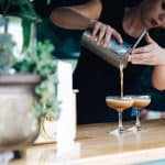The speakeasy Hotel female bartender straining espresso martinis from boston shaker into champagne saucer style glasses
